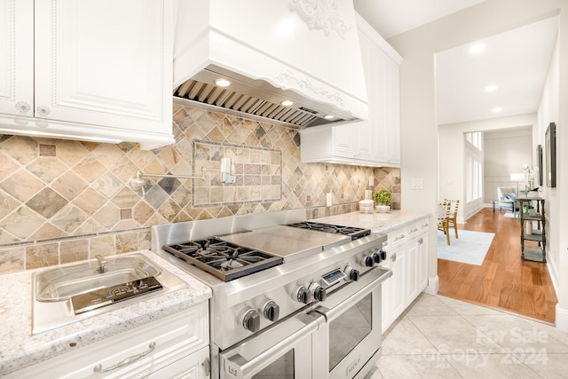 kitchen featuring custom exhaust hood, backsplash, white cabinetry, double oven range, and light wood-type flooring