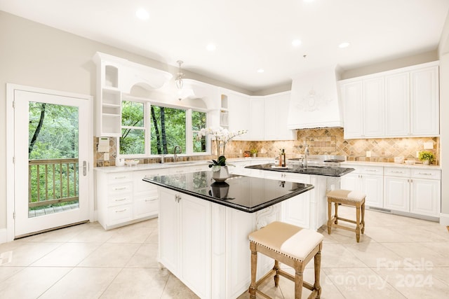 kitchen with custom range hood, light tile patterned flooring, white cabinets, a breakfast bar area, and a center island