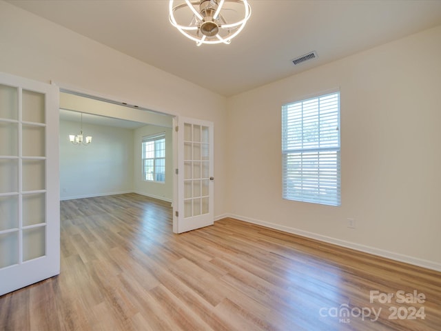 empty room with a healthy amount of sunlight, french doors, light wood-type flooring, and an inviting chandelier