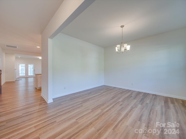 spare room featuring an inviting chandelier, light hardwood / wood-style flooring, and french doors