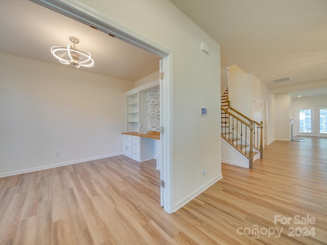 interior space with built in desk, a notable chandelier, light hardwood / wood-style flooring, and built in shelves