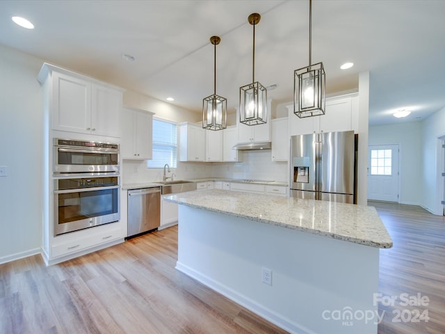 kitchen with appliances with stainless steel finishes, light wood-type flooring, a kitchen island, decorative light fixtures, and white cabinets