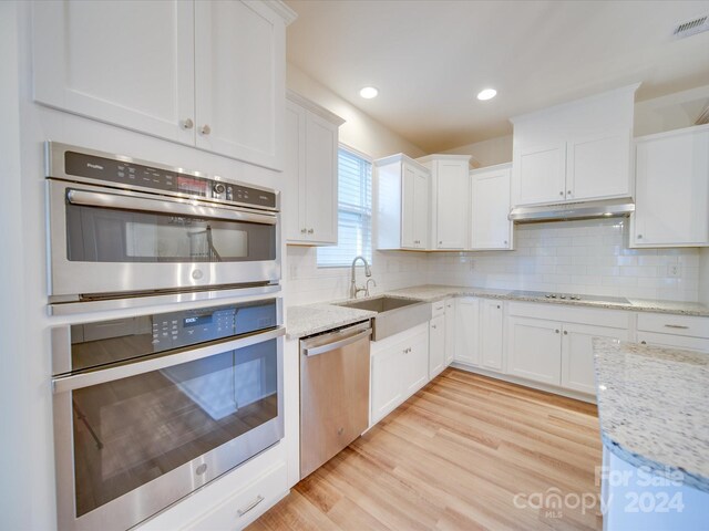 kitchen featuring appliances with stainless steel finishes, light wood-type flooring, white cabinetry, and tasteful backsplash