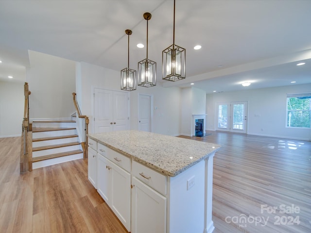 kitchen featuring a kitchen island, hanging light fixtures, light wood-type flooring, white cabinetry, and light stone counters