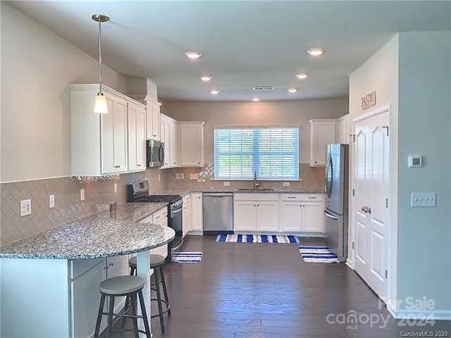 kitchen with appliances with stainless steel finishes, dark wood-type flooring, white cabinets, decorative light fixtures, and sink