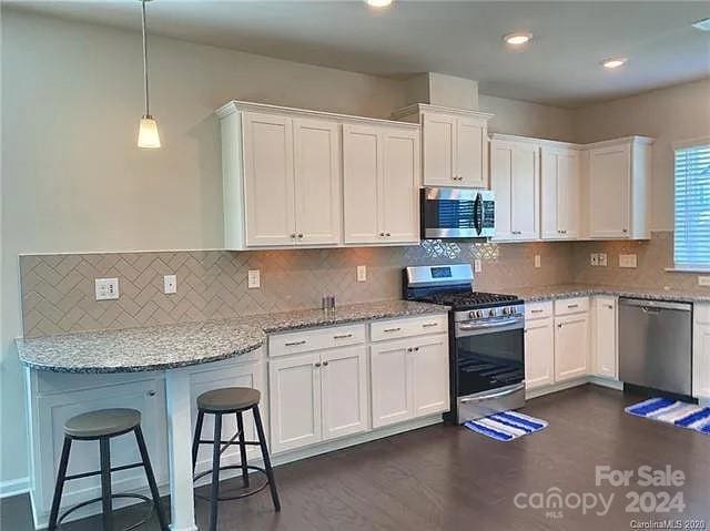 kitchen featuring a breakfast bar, white cabinets, light stone countertops, pendant lighting, and stainless steel appliances