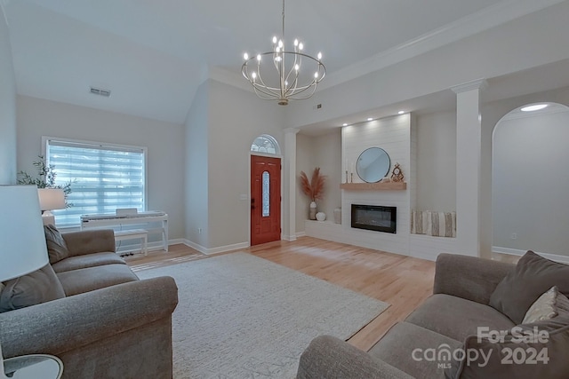 living room featuring light hardwood / wood-style floors, ornamental molding, a large fireplace, a notable chandelier, and ornate columns