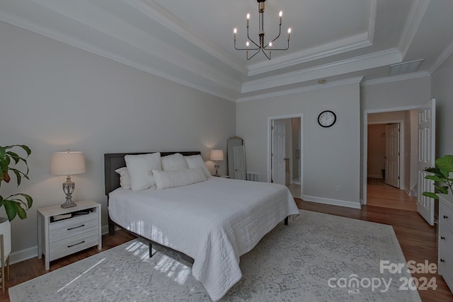 bedroom featuring crown molding, a tray ceiling, hardwood / wood-style floors, a chandelier, and ensuite bath