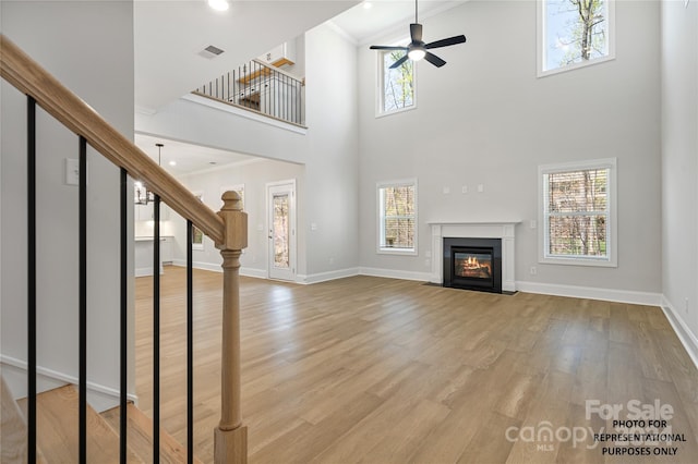 unfurnished living room with ceiling fan, light wood-type flooring, ornamental molding, and a high ceiling