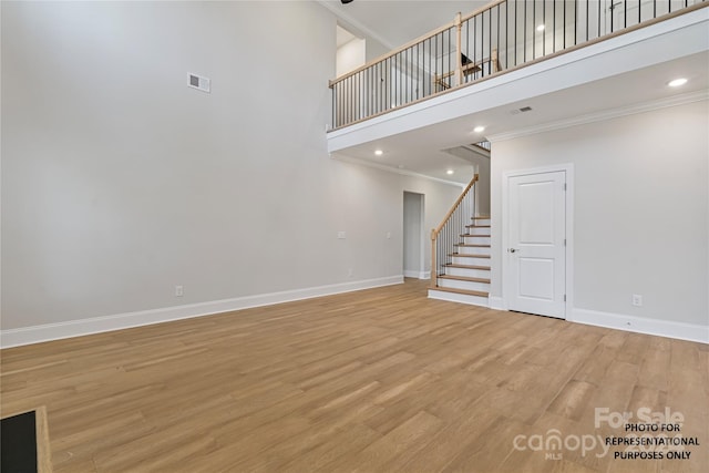 unfurnished living room featuring crown molding, a towering ceiling, visible vents, stairway, and baseboards