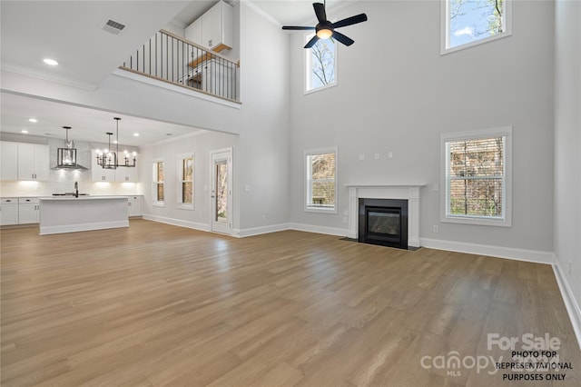 unfurnished living room featuring light wood-type flooring, a towering ceiling, ceiling fan with notable chandelier, and ornamental molding