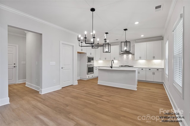 kitchen featuring appliances with stainless steel finishes, wall chimney range hood, white cabinets, light hardwood / wood-style floors, and hanging light fixtures