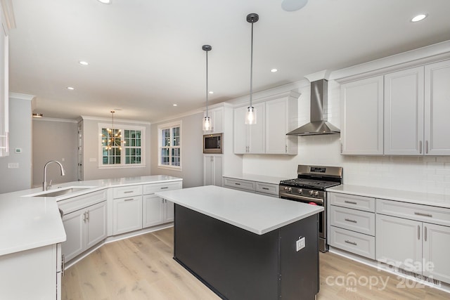 kitchen with sink, hanging light fixtures, a kitchen island, wall chimney exhaust hood, and appliances with stainless steel finishes