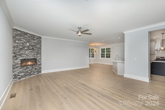 unfurnished living room featuring light hardwood / wood-style flooring, crown molding, ceiling fan with notable chandelier, and a stone fireplace