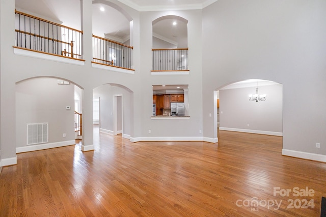 unfurnished living room featuring a notable chandelier, a towering ceiling, light hardwood / wood-style floors, and crown molding