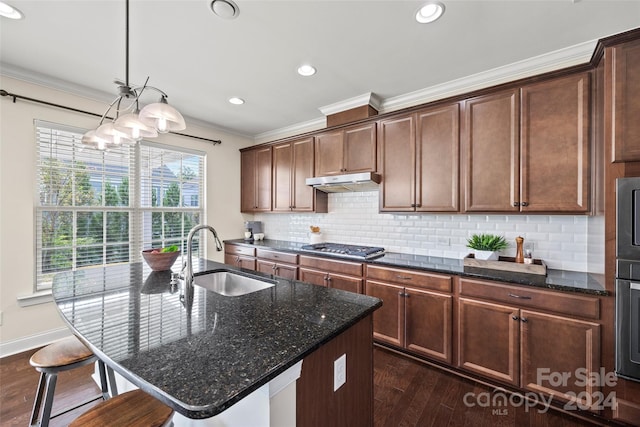 kitchen with dark stone countertops, dark wood-type flooring, a kitchen island with sink, and sink