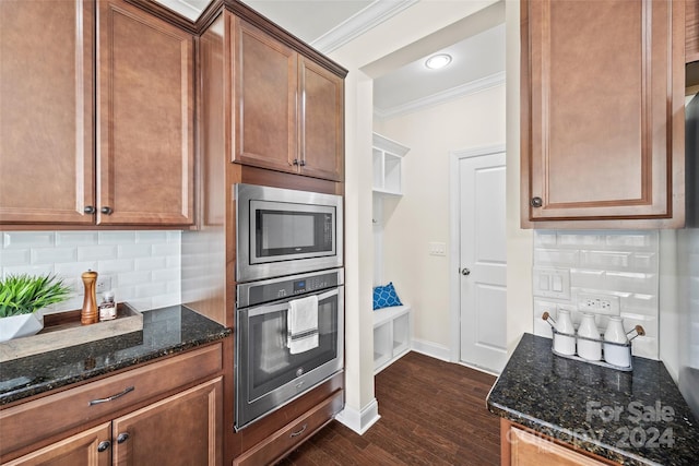 kitchen featuring appliances with stainless steel finishes, dark wood-type flooring, tasteful backsplash, crown molding, and dark stone counters