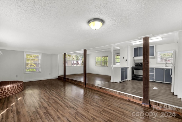 unfurnished living room featuring a textured ceiling, a healthy amount of sunlight, sink, and dark wood-type flooring