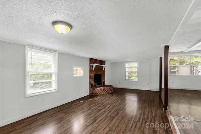 unfurnished living room with a textured ceiling, dark wood-type flooring, and a brick fireplace