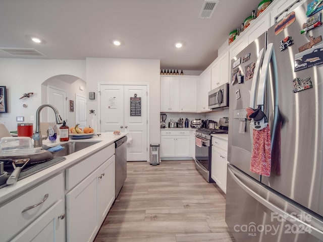 kitchen with sink, white cabinetry, appliances with stainless steel finishes, light wood-type flooring, and decorative backsplash