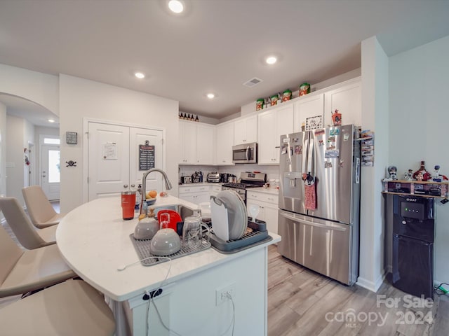 kitchen featuring white cabinets, a center island with sink, appliances with stainless steel finishes, and light wood-type flooring