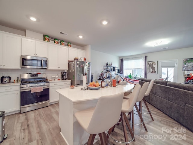 kitchen featuring a center island with sink, white cabinetry, appliances with stainless steel finishes, a breakfast bar area, and light wood-type flooring