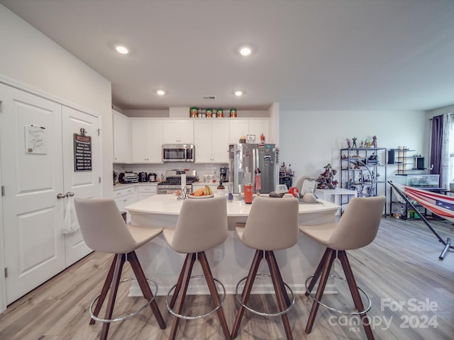 kitchen with appliances with stainless steel finishes, light wood-type flooring, a breakfast bar area, and white cabinets