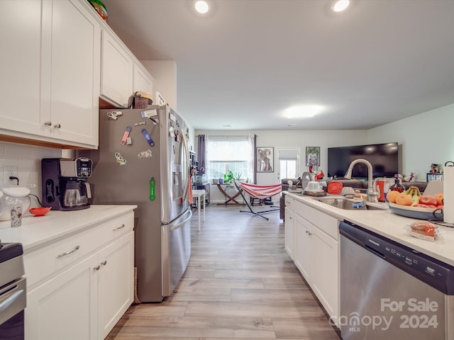 kitchen with appliances with stainless steel finishes, decorative backsplash, white cabinetry, light wood-type flooring, and sink