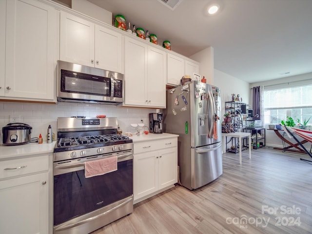 kitchen featuring white cabinets, backsplash, appliances with stainless steel finishes, and light wood-type flooring