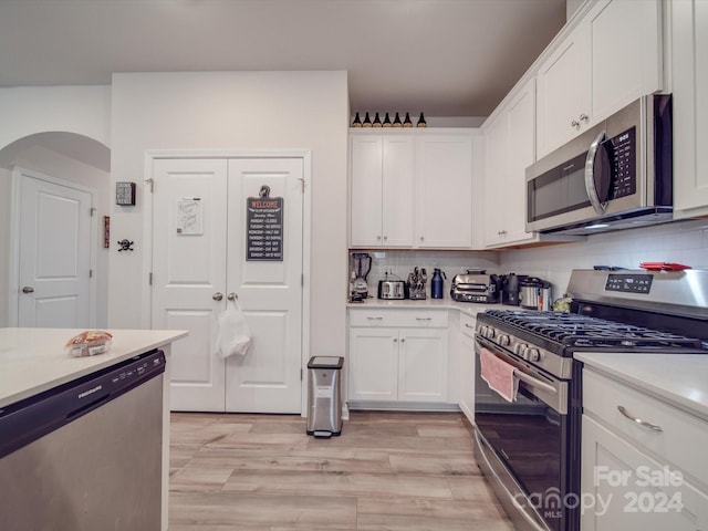 kitchen with decorative backsplash, white cabinets, light hardwood / wood-style floors, and appliances with stainless steel finishes