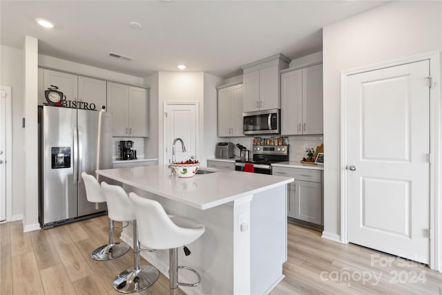 kitchen with a kitchen island with sink, stainless steel appliances, light wood-type flooring, and gray cabinets