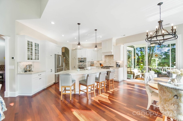 kitchen with white cabinets, a center island with sink, decorative light fixtures, backsplash, and dark wood-type flooring