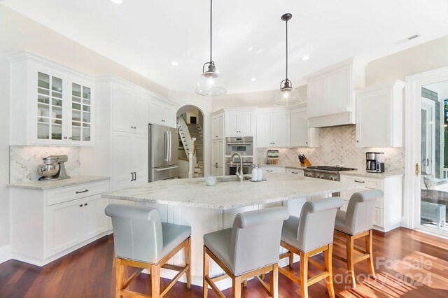 kitchen featuring pendant lighting, dark hardwood / wood-style flooring, a center island with sink, stainless steel appliances, and white cabinetry