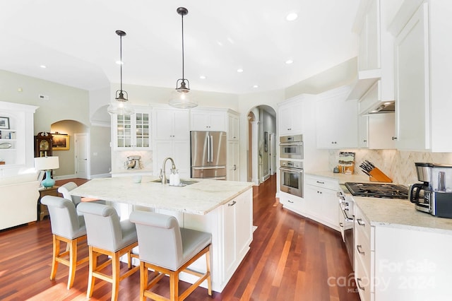 kitchen with pendant lighting, dark wood-type flooring, a center island with sink, sink, and stainless steel appliances