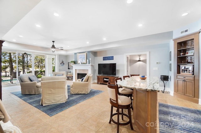 living room featuring ceiling fan, a tile fireplace, and light tile patterned floors