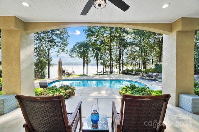 view of swimming pool with a water view, ceiling fan, and a patio