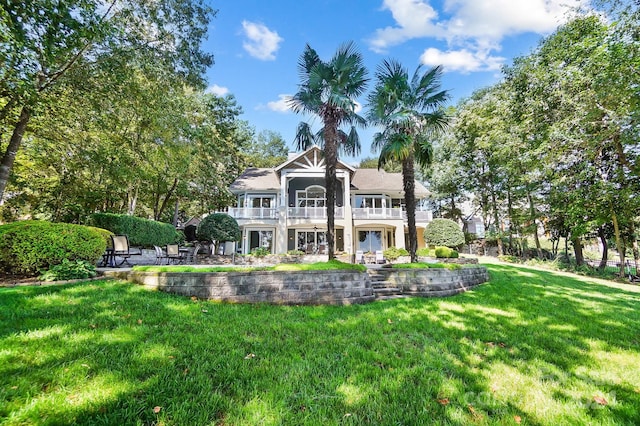 rear view of property featuring a patio area, a balcony, and a lawn