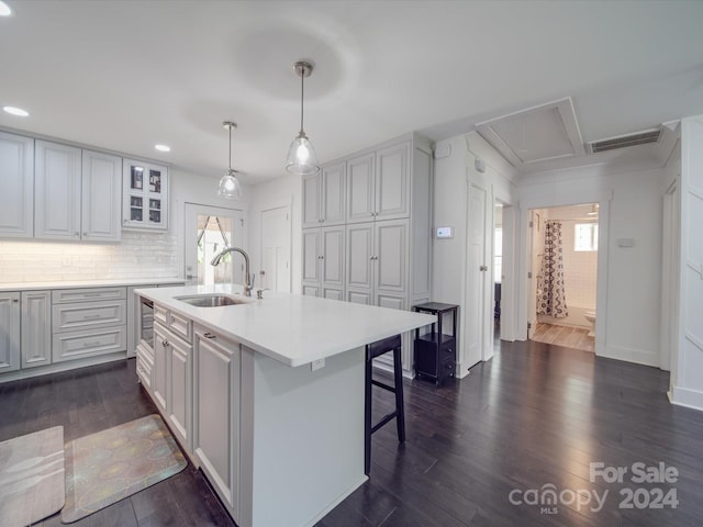 kitchen featuring sink, decorative light fixtures, a kitchen island with sink, dark wood-type flooring, and a kitchen bar