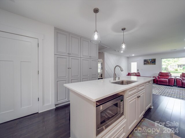 kitchen with pendant lighting, sink, a kitchen island with sink, dark hardwood / wood-style floors, and stainless steel microwave