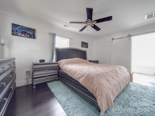 bedroom with ceiling fan, a barn door, and dark wood-type flooring