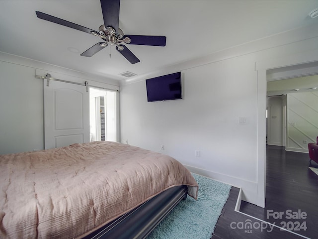 bedroom with a barn door, dark hardwood / wood-style floors, and ceiling fan