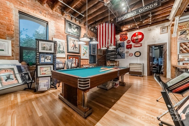 game room featuring a towering ceiling, pool table, brick wall, and hardwood / wood-style floors