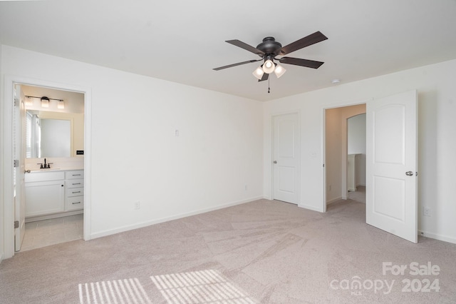 unfurnished bedroom featuring light carpet, ensuite bath, sink, and ceiling fan