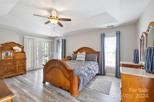 bedroom with ceiling fan, a tray ceiling, and multiple windows