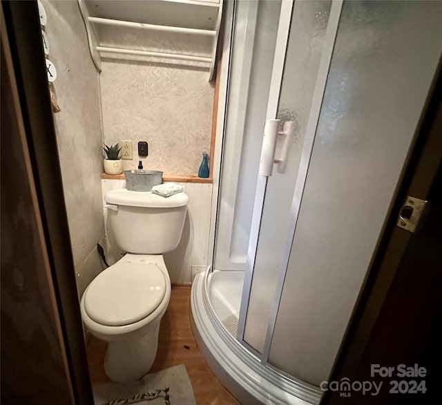 bathroom with hardwood / wood-style floors, toilet, and a shower with door