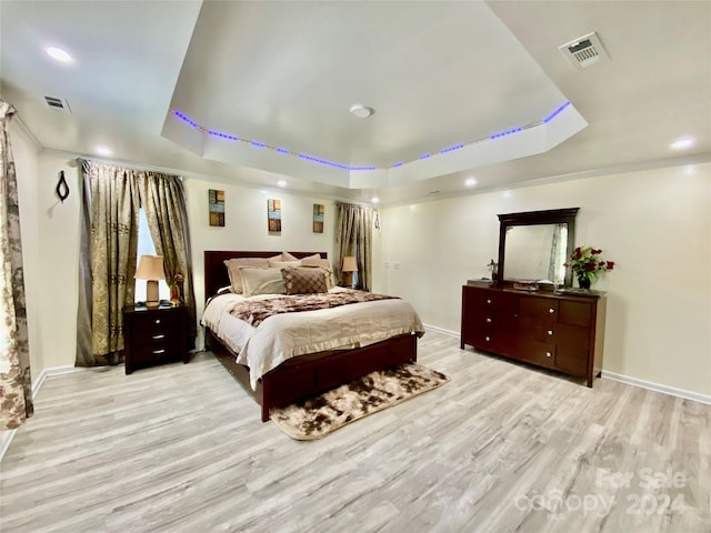 bedroom with ornamental molding, a tray ceiling, and light hardwood / wood-style flooring