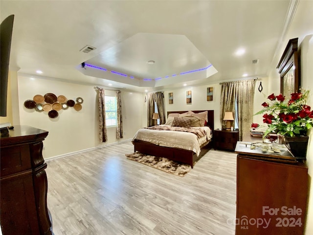 bedroom featuring light wood-type flooring, crown molding, and a raised ceiling