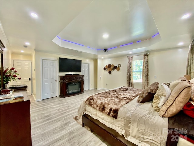 bedroom with light wood-type flooring, ornamental molding, and a tray ceiling