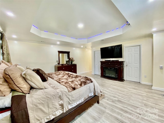 bedroom with light hardwood / wood-style flooring, a tray ceiling, and ornamental molding