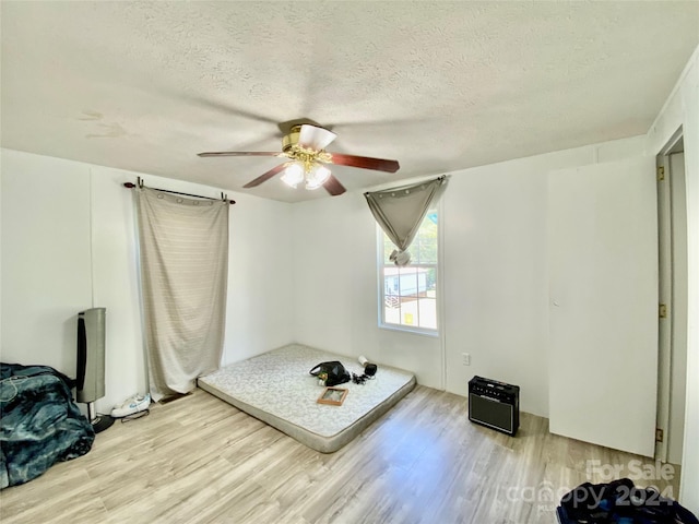 workout area with ceiling fan, a textured ceiling, and light hardwood / wood-style floors